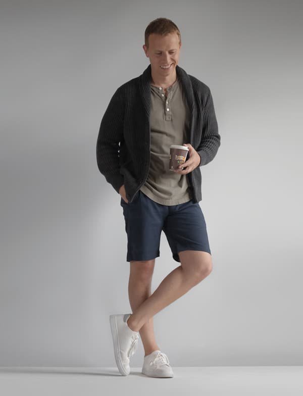a man wearing a shawl collar cardigan over a henley shirt and well fitting shorts with low top sneakers