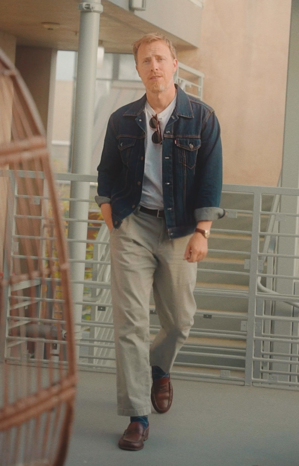 A man wearing a denim jacket, white t-shirt, chino pants, and loafers