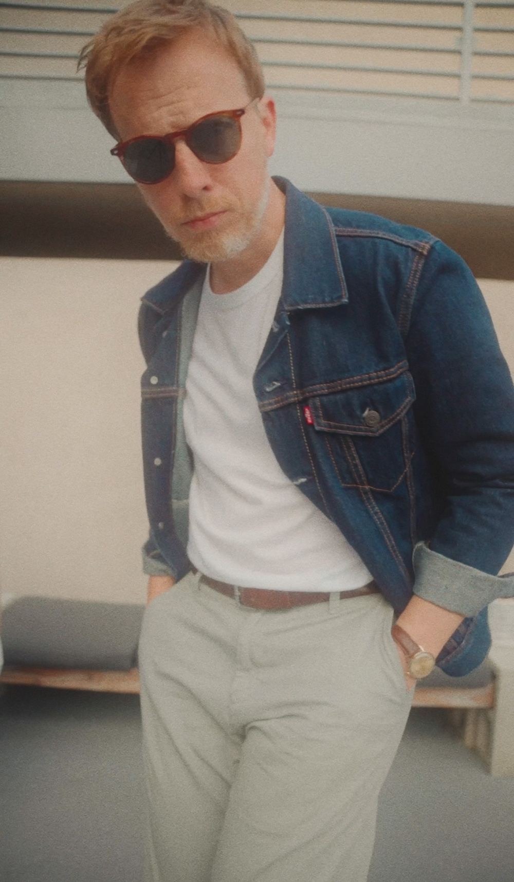 Close up of a man wearing a denim jacket, white t-shirt and chino pants