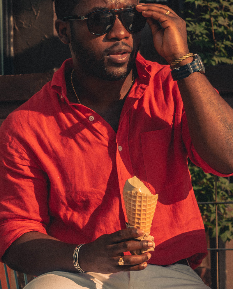 man wearing a linen shirt with gold necklace, aviator sunglasses, watch, and two bracelets
